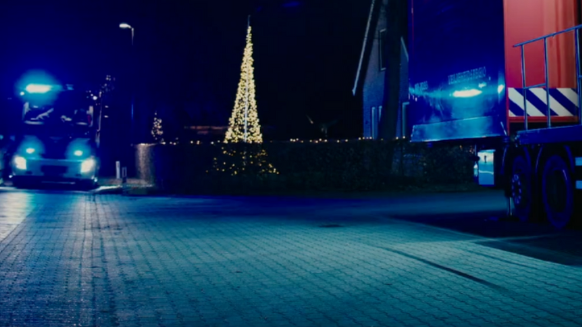 afbeelding van brandweer met blauwe lampen aan in het donker, op straat met kerstboom met lichtjes